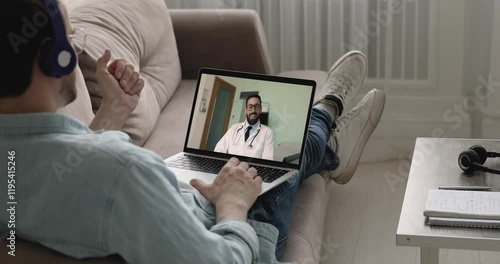 Man patient settled down on couch engaging in videocall on laptop, smiling young 35s doctor in white coat provide telemedicine consultation, virtual health checkup. Telemedicine and remote healthcare photo