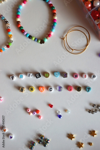 Friendship bracelet spelled with letter beads. Colorful handmade bracelets and various jewelry making supplies. Top view, white background.