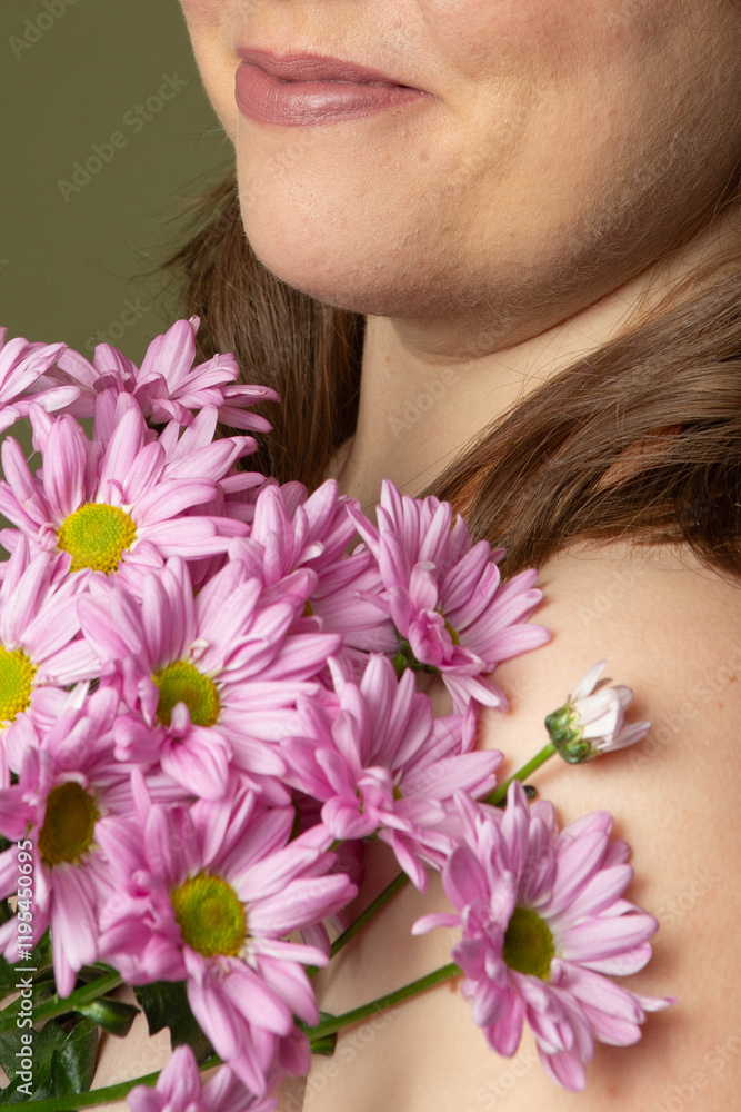 Fototapeta premium Curvy woman with clear skin imperfections in studio, purple daisy flowers and green background, unrecognizable