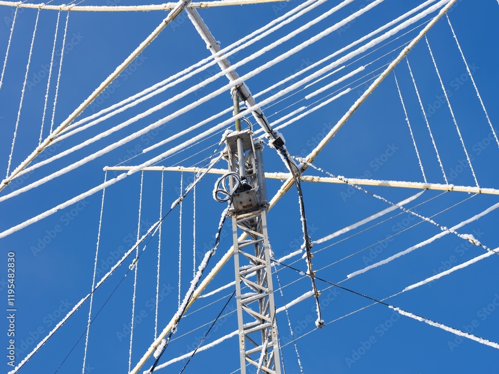 Close-up shot of a ham radio antenna covered in snow against a blue sky. Close-up shot of a ham radio antenna covered in snow against a blue sky.
