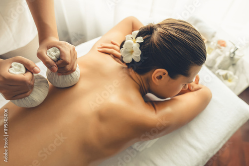 Hot herbal ball spa massage body treatment, masseur gently compresses herb bag on woman body. Tranquil and serenity of aromatherapy recreation in day lighting ambient at spa salon. Quiescent photo