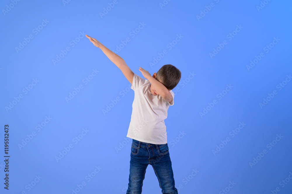 Little carefree boy with arms raised dancing and dabbing while standing on isolated blue background Little carefree boy with arms raised dancing and dabbing while standing on isolated blue background