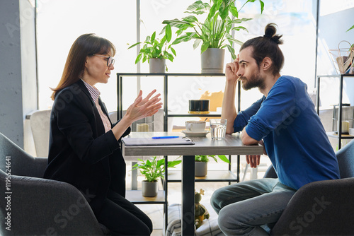 Middle aged female mental health specialist, insurance agent working with young male photo