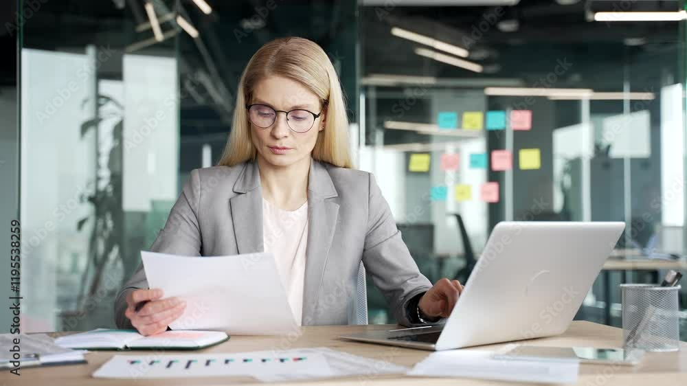 Confident businesswoman in a suit analyzing financial documents checking data on laptop while sitting at desk at a workplace in a business office. Busy female financier deals with financial report Confident businesswoman in a suit analyzing financial documents checking data on laptop while sitting at desk at a workplace in a business office. Busy female financier deals with financial report