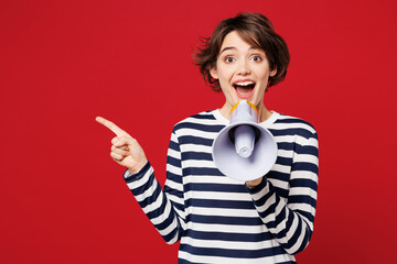 Young surprised woman wear blue striped sweatshirt casual clothes hold in hand megaphone scream announces discounts sale Hurry up isolated on plain red background studio portrait. Lifestyle concept.