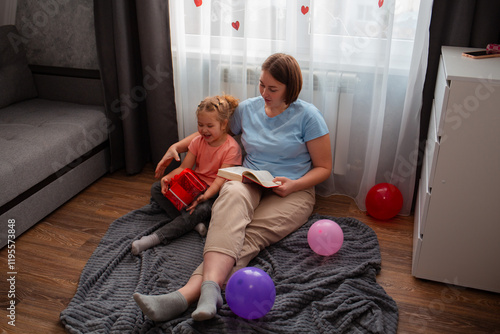 Wide shot of young Caucasian woman reads a book of fairy tales to her child. Preschool-age girl is interested in spending time with her mom. Concept of mother's day photo