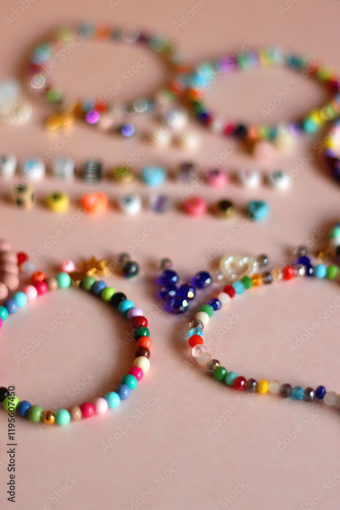 Friendship bracelet spelled with letter beads. Colorful handmade bracelets and various beads. Selective focus, pink background.