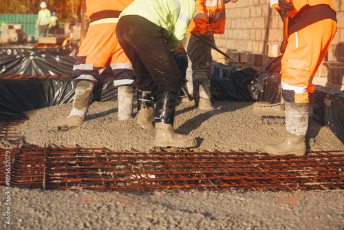 Construction workers laying concrete at building site in bright orange safety gear during daylight hours photo