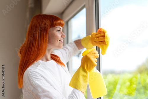 Woman cleaning windows with a spray bottle and cloth on a sunny day indoors photo