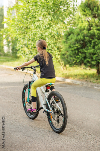 Preteen girl riding bicycle along tree-lined path during sunny weather photo