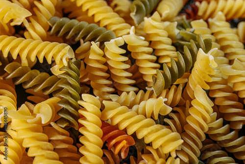 A colorful close-up of dry spiral pasta in vibrant orange, yellow, and green hues, highlighting its texture and shape. Ideal for food-related themes and culinary content. photo