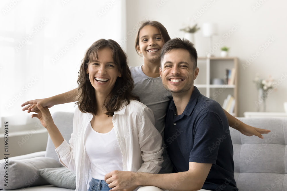 Portrait of happy playful family with adorable little daughter, sit together on cozy sofa, laughing, smiling, looking at camera, posing for photo, enjoy active leisure, playtime in modern living room Portrait of happy playful family with adorable little daughter, sit together on cozy sofa, laughing, smiling, looking at camera, posing for photo, enjoy active leisure, playtime in modern living room