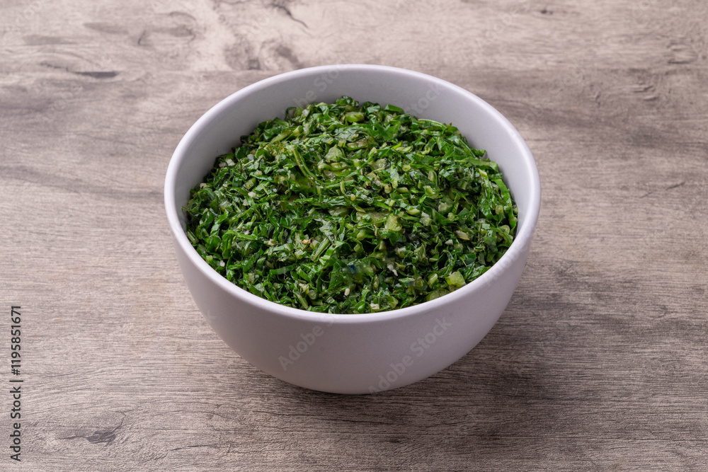Cooked kale strips, typical brazilian feijoada sidedish in a bowl over wooden table Cooked kale strips, typical brazilian feijoada sidedish in a bowl over wooden table