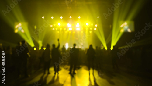 Dancing people on the nightclub's dancefloor at the part, concert venue, afterparty under the yellow beams of the spotlights of the light show. Blurred shot photo