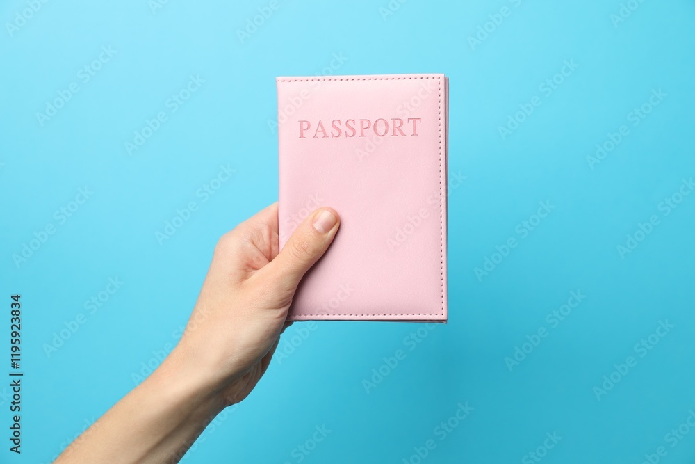 Fototapeta premium Woman holding passport in bright cover on light blue background, closeup