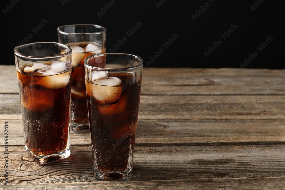 Refreshing cola with ice cubes in glasses on wooden table against black background, closeup. Space for text Refreshing cola with ice cubes in glasses on wooden table against black background, closeup. Space for text