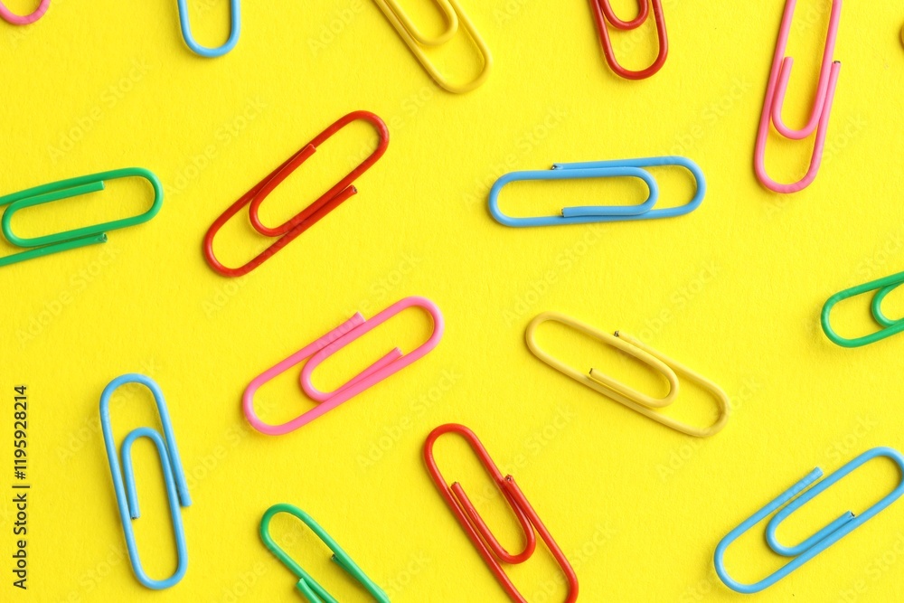 Colorful paper clips on yellow background, flat lay Colorful paper clips on yellow background, flat lay