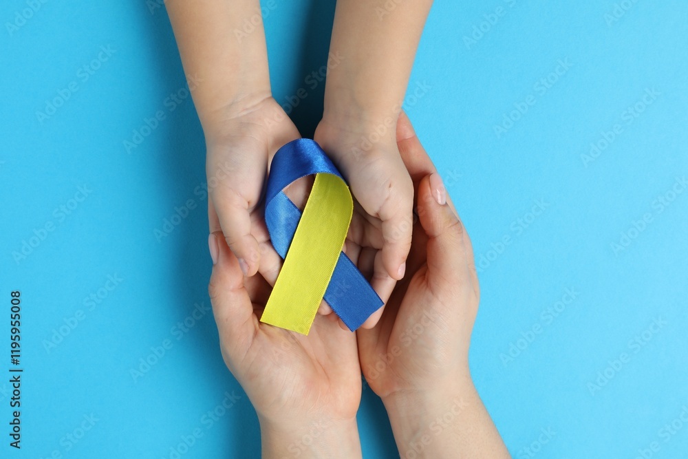 Φωτογραφία Woman with child holding yellow and blue ribbons on color background, top view