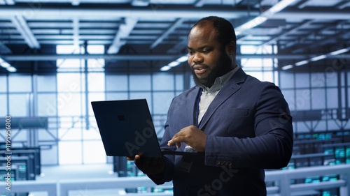 Programmer in data center typing on laptop, running error checking utilities. IT professional in server room looking for network issues affecting rigs performance using digital device, camera A