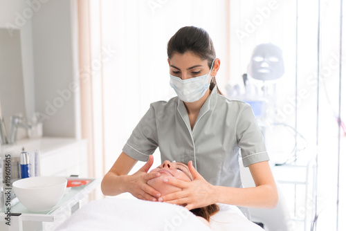 Foto Female massage therapist massaging woman's face at cosmetology salon