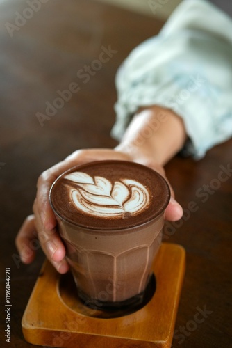 An asian woman are holding a glass of hot chocolate drink. Glass with wooden coaster on the table. Minuman coklat photo