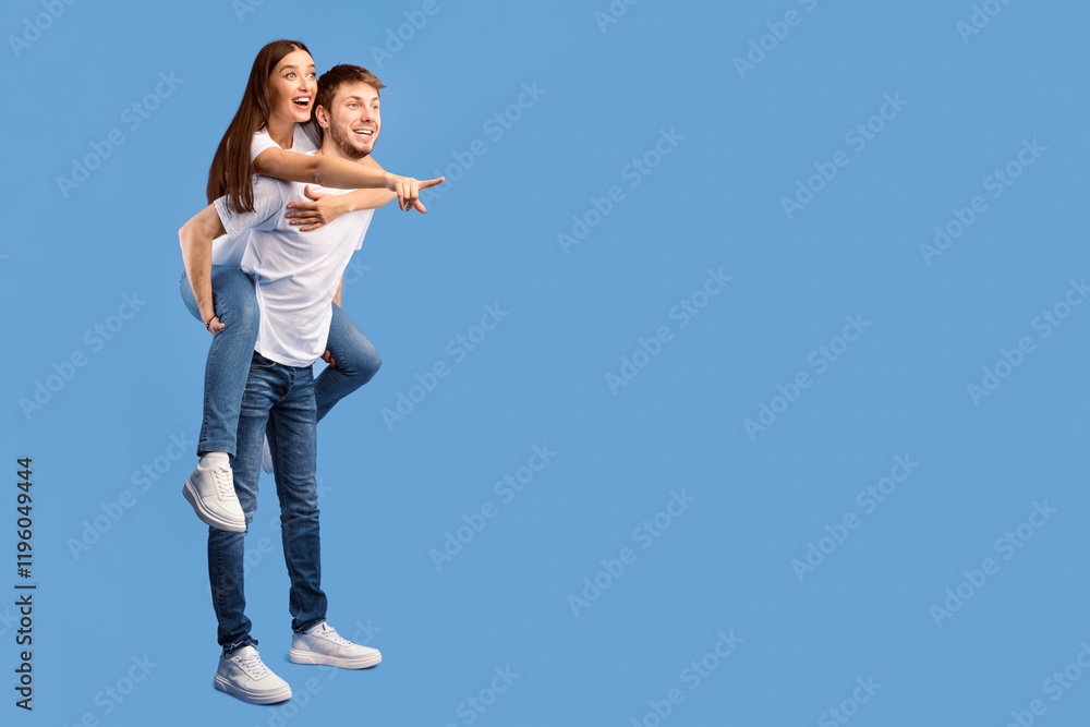 Surprised couple pointing finger aside at copy space isolated over purple studio wall, boy giving his girl piggyback ride Surprised couple pointing finger aside at copy space isolated over purple studio wall, boy giving his girl piggyback ride