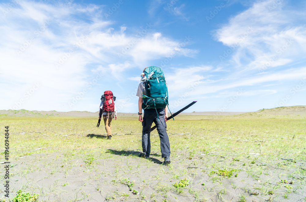 Two people with backpacks trekking across scenic sand dunes, enjoying the adventure and connection with nature under an open sky.