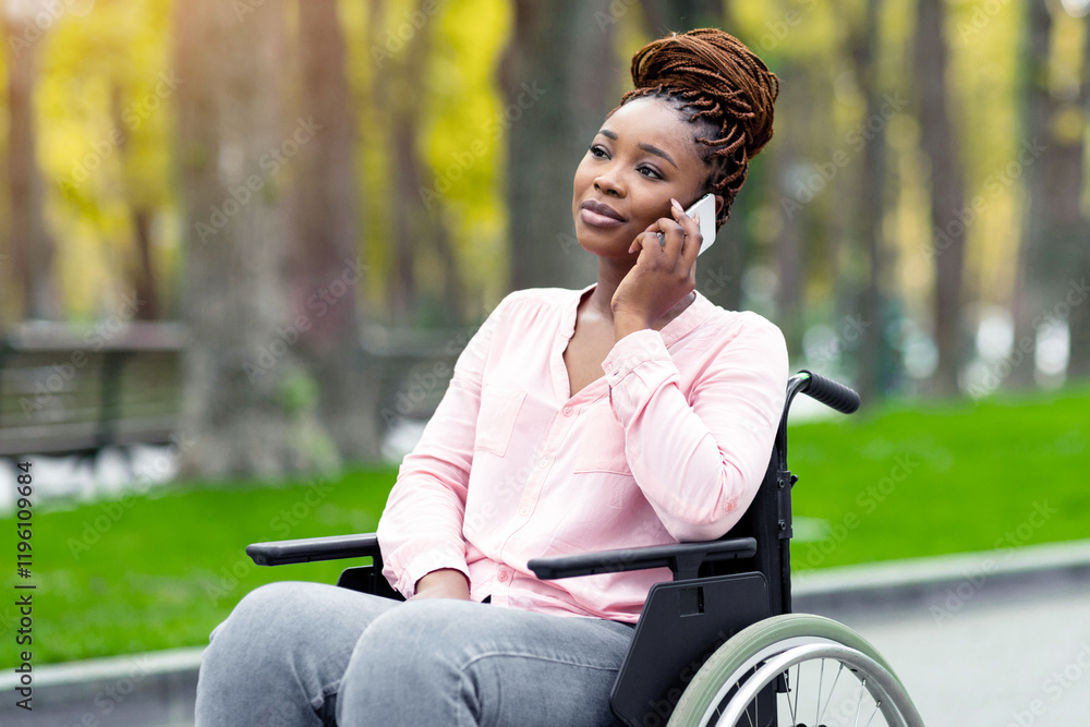 Young Afro lady in wheelchair having phone conversation at city park in autumn. Disabled black woman with smartphone talking to friend, enjoying remote communication outdoors during fall season Young Afro lady in wheelchair having phone conversation at city park in autumn. Disabled black woman with smartphone talking to friend, enjoying remote communication outdoors during fall season