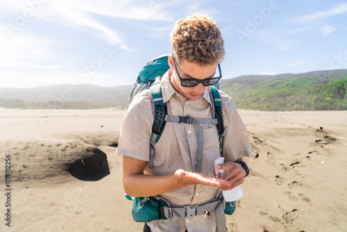 Obraz na płótnie A young mountaineer preparing for the hike by applying sunscreen, ensuring protection from the sun during the outdoor adventure. w salonie