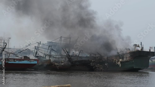 Thick black smoke and flames from several fishing boats burning on the dock.