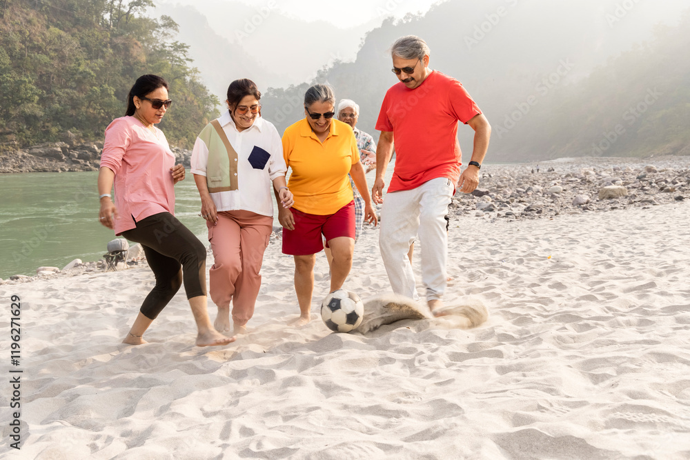 Fototapeta premium Group of senior friends playing football at sandy beach together