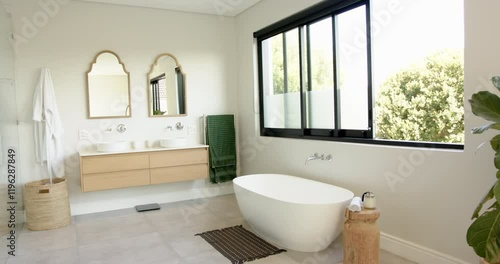Modern bathroom with freestanding bathtub, double sink vanity, and large window, copy space