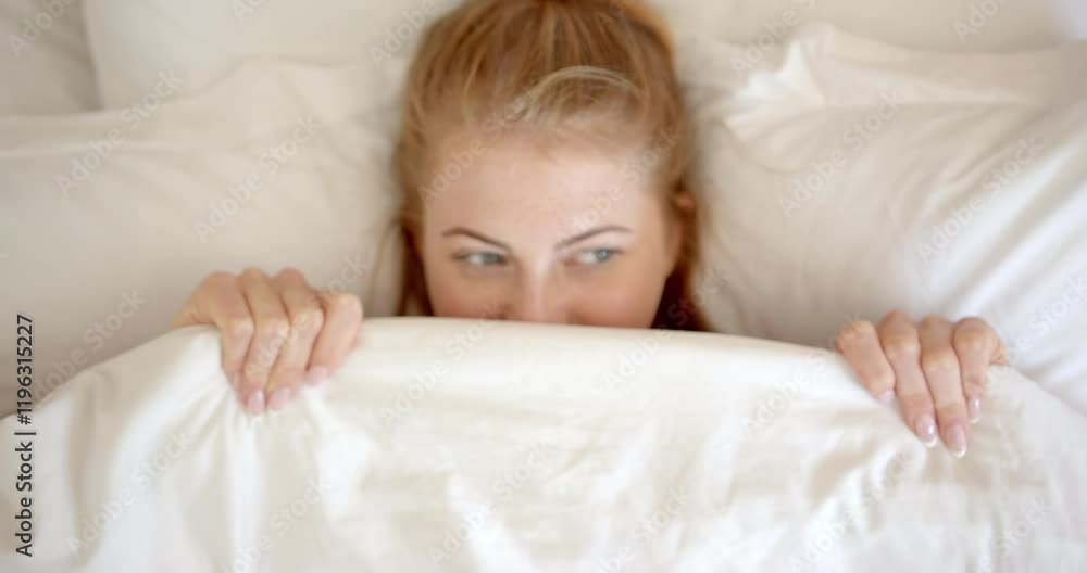 Woman peeking from under blanket, relaxing in bed at home Woman peeking from under blanket, relaxing in bed at home