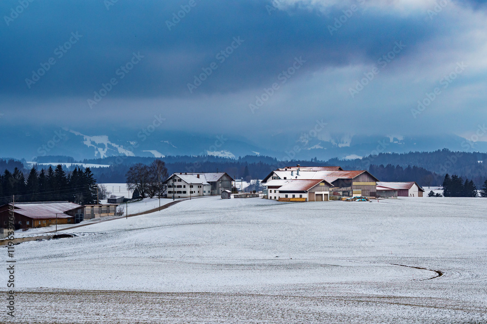 Panoramic view over snow-covered fields and a village on Allgäu mountains in winter. Cloudy, foggy sky Panoramic view over snow-covered fields and a village on Allgäu mountains in winter. Cloudy, foggy sky