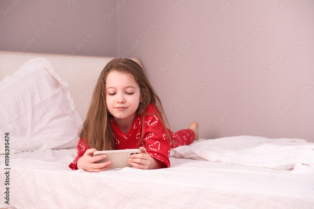 A Child is Relaxing Comfortably on the Bed with a Smartphone in Hand, Enjoying Leisure Time A Child is Relaxing Comfortably on the Bed with a Smartphone in Hand, Enjoying Leisure Time