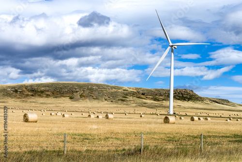 Agricultural field with bales of hay and wind power tower turbine at fall season
