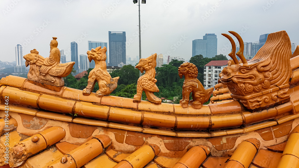 Obraz premium Thean Hou temple roof adorned with intricate, terracotta sculptures. Creatures, mythical beasts or guardians, stand along edge of roof against backdrop of modern city skyline of Kuala Lumpur, Malaysia