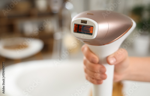 Female hand with modern photoepilator in bathroom, closeup photo