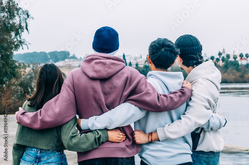 Canvas Print Four young multiracial friends are hugging each other while looking at the river