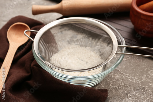 Metal sieve in bowl with flour and kitchen utensils on grunge background, closeup