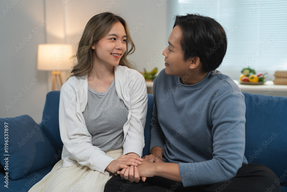 Happy young asian couple sitting on the sofa in their cozy living room, holding hands and engaging in cheerful conversation, enjoying quality time and deepening their bond Happy young asian couple sitting on the sofa in their cozy living room, holding hands and engaging in cheerful conversation, enjoying quality time and deepening their bond