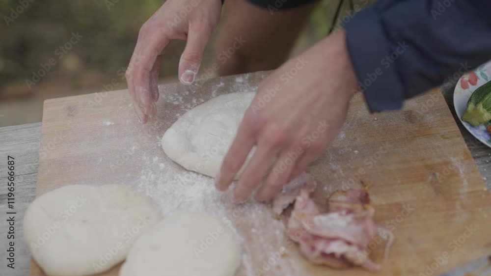 A person is making a pizza with bacon and cheese. The pizza is on a wooden cutting board A person is making a pizza with bacon and cheese. The pizza is on a wooden cutting board