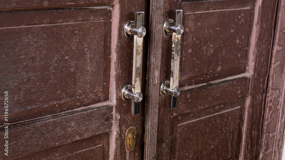 Obraz premium Close-up of a rustic wooden door with metal handles showing signs of wear and rust