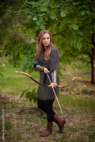 A young woman warrior with wavy hair and in chain mail armor holds a bow with arrows in her hands. photo