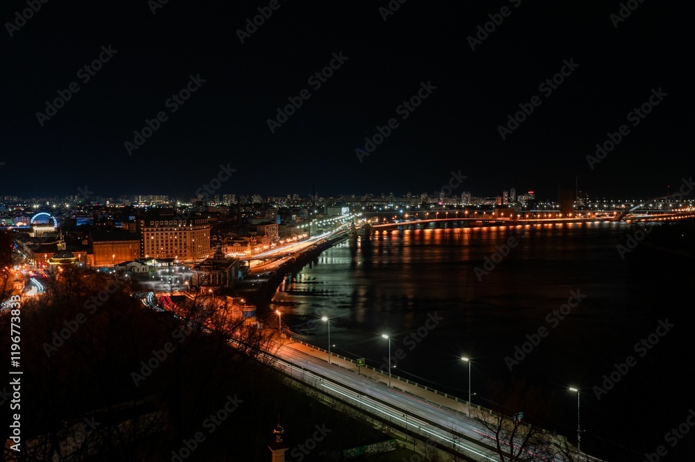 Fototapeta premium Cityscape at night with illuminated bridge and river reflections.