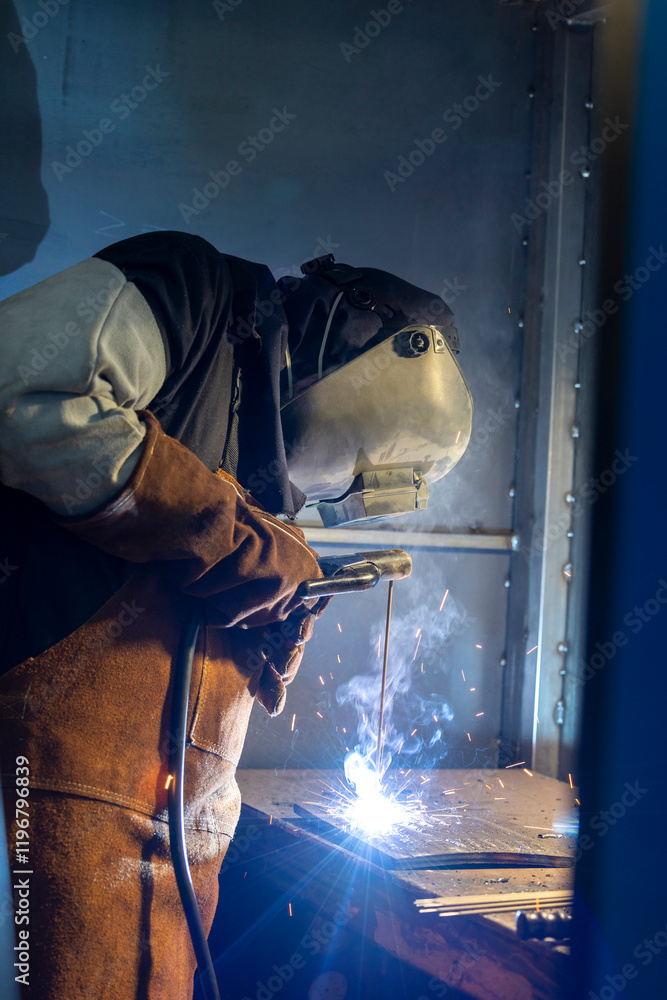 Fototapeta premium A skilled welder is intensely focused on welding metal pieces, showcasing the sparks and bright light characteristic of the welding process in an industrial environment.