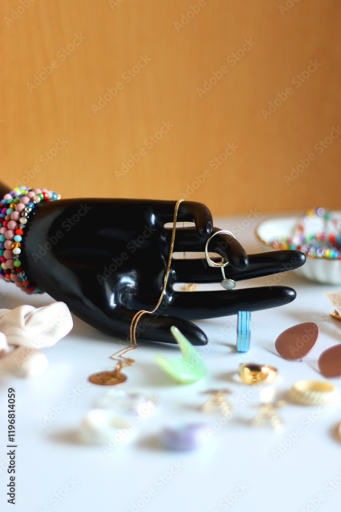 Hand figurine, sunglasses, gold jewelry, colorful bead jewelry, statement rings and various hair accessories on the white table. Selective focus.