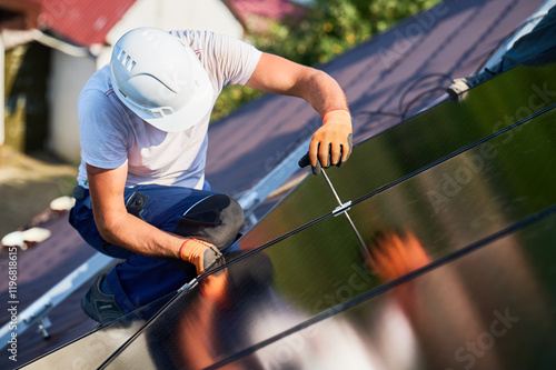 Worker building photovoltaic solar panel system on rooftop of house. Man engineer in helmets and gloves installing solar module with help of hex key outdoors. Renewable energy generation concept. photo