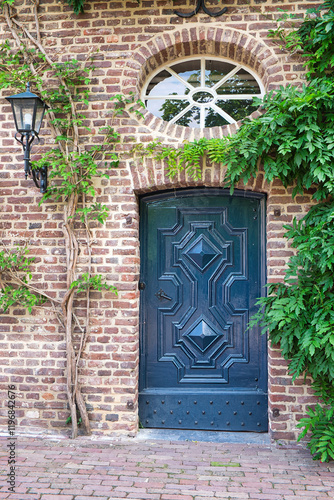 Beautiful dark blue-painted entrance door of an old farmhouse, framed by non-blooming wisteria plants in June, with a round window and an old lamp. Germany, Schwalmtal near Moenchengladbach photo