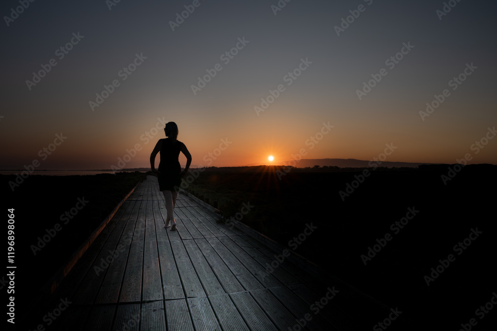Silhouette of a Woman Walking on a Wooden Path at Sunset Silhouette of a Woman Walking on a Wooden Path at Sunset